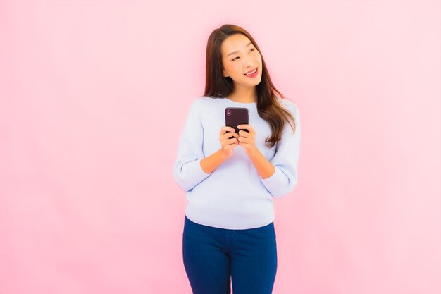 Retrato de uma bela jovem asiática usando telefone celular inteligente na parede isolada de cor rosa