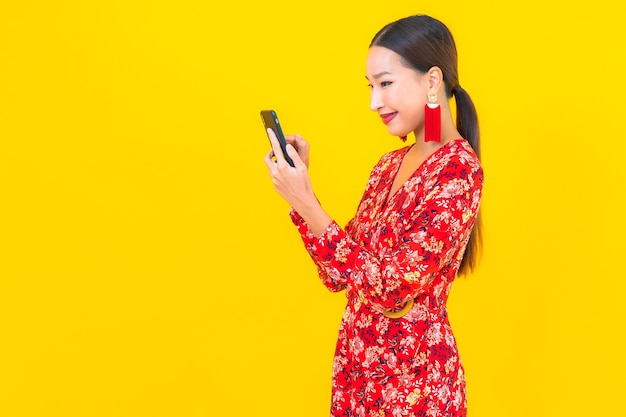 Retrato de uma bela jovem asiática usando um telefone celular inteligente na parede amarela