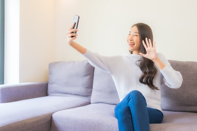 Retrato de uma bela jovem asiática usando um telefone celular inteligente no sofá no interior da sala de estar