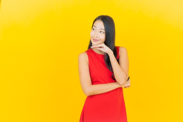 Retrato de uma bela jovem asiática usando um vestido vermelho e sorrindo com ação na parede amarela