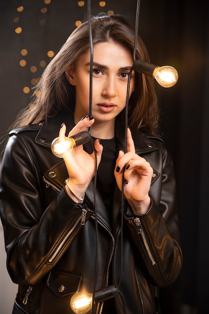 Retrato de uma bela jovem modelo na jaqueta de couro preta se passando perto de lâmpadas.