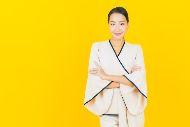 Retrato de uma bela jovem mulher asiática de negócios sorrindo com um terno branco na parede amarela