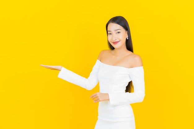 Retrato de uma bela jovem mulher asiática de negócios sorrindo com um vestido branco na parede amarela