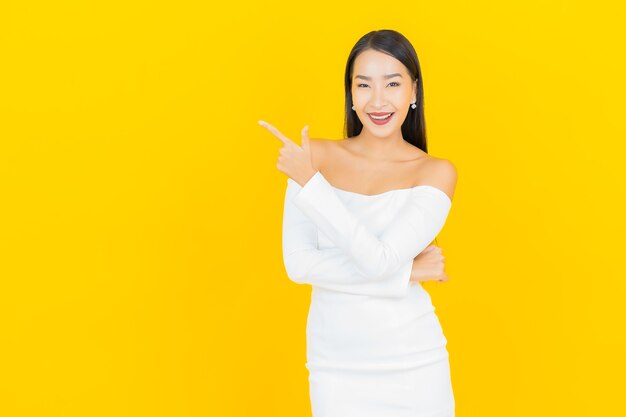 Retrato de uma bela jovem mulher asiática de negócios sorrindo com um vestido branco na parede amarela