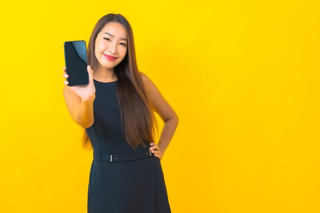 Retrato de uma bela jovem mulher de negócios asiática com uma xícara de café e um celular inteligente em fundo amarelo.