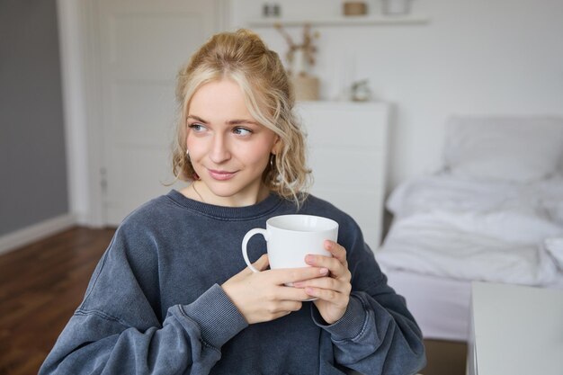 Foto grátis retrato de uma bela jovem sorridente sentada no quarto com uma chávena de chá descansando em casa sozinha