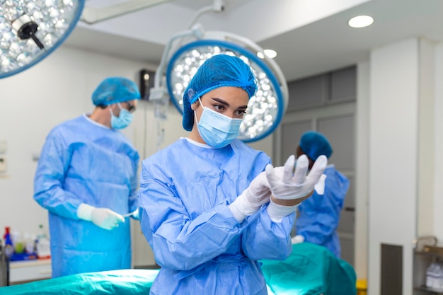 Retrato de uma bela médica cirurgiã colocando luvas médicas em pé na sala de operação Cirurgião na moderna sala de cirurgia