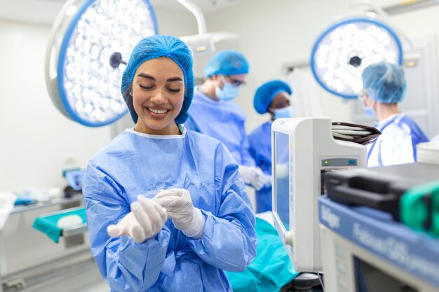 Retrato de uma bela médica cirurgiã colocando luvas médicas em pé na sala de operação Cirurgião na moderna sala de cirurgia