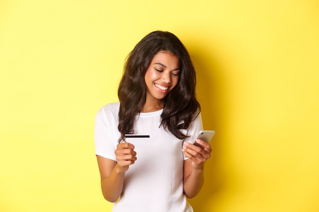 Retrato de uma bela mulher afro-americana, compras online com smartphone e suporte de cartão de crédito ...