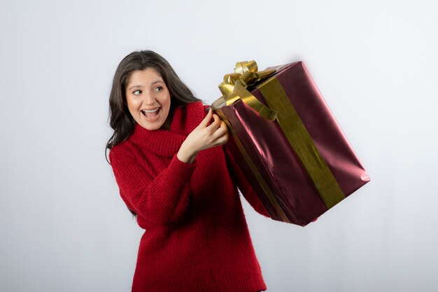 Retrato de uma bela mulher sorridente no suéter vermelho segurando uma caixa de presente de Natal.
