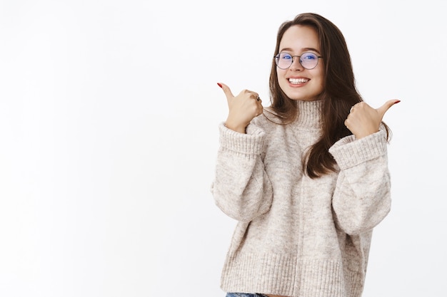 Retrato de uma cliente feminina satisfeita e satisfeita, de suéter e óculos fazendo sinal de positivo