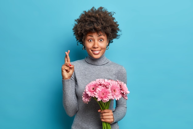 Retrato de uma cruz negra afro-americana positiva acredita que os sonhos se tornam realidade segura um buquê de gérberas rosa