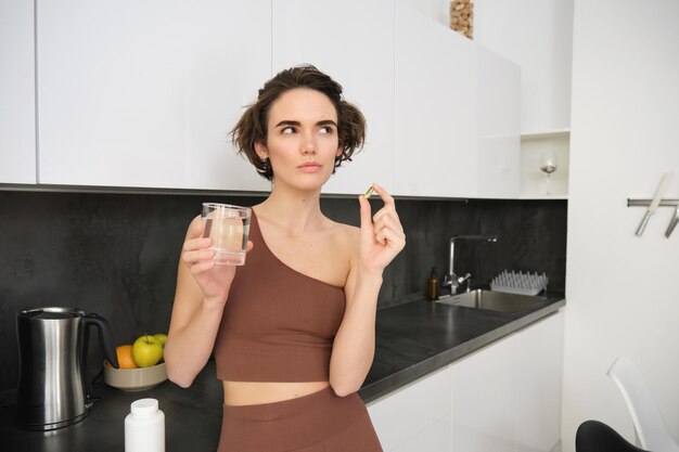 Retrato de uma desportista a beber água, a tomar vitaminas e suplementos dietéticos para uma pele saudável
