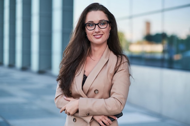 Foto grátis retrato de uma empresária de sucesso com um sorriso encantador posando na rua com arquitetura interessante ao fundo.