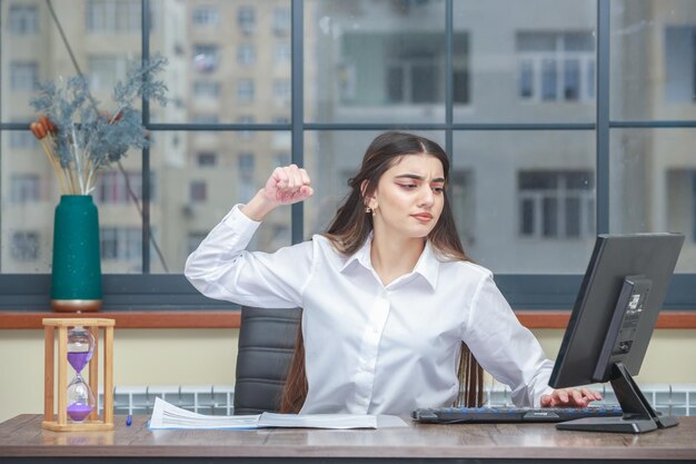 Retrato de uma empresária zangada sentada à mesa e apontar o punho para o pc