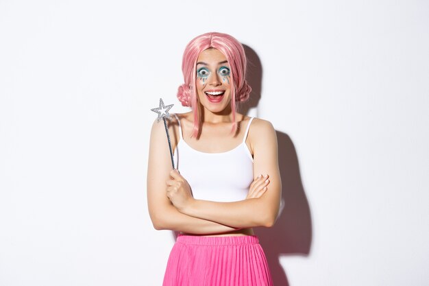 Retrato de uma garota atraente com peruca rosa e maquiagem brilhante, vestida como uma fada para a festa de halloween, segurando a varinha mágica e sorrindo.