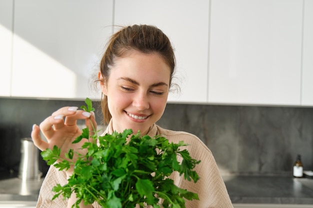 Retrato de uma garota atraente com um monte de salsa comendo ervas frescas e legumes cozinhando no