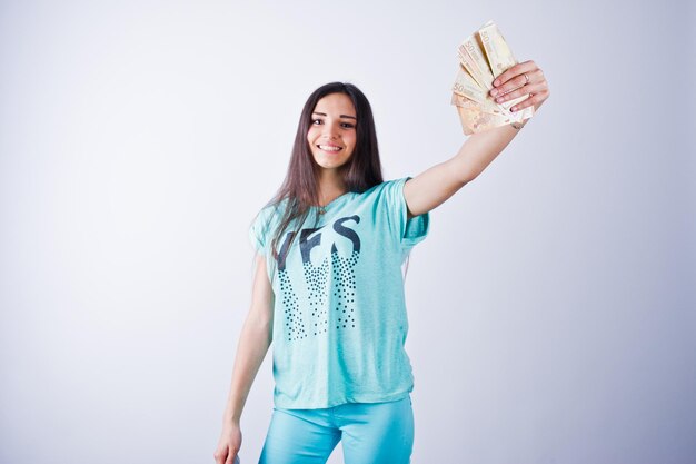 Retrato de uma garota atraente em camiseta azul ou turquesa e calças posando com muito dinheiro na mão