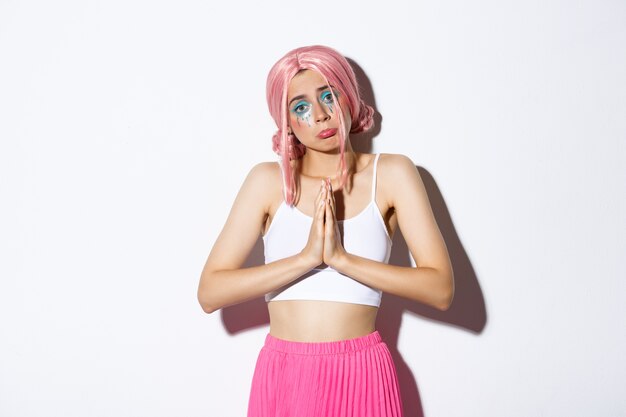 Retrato de uma garota boba e triste com uma peruca rosa anime pedindo ajuda, de mãos dadas em oração