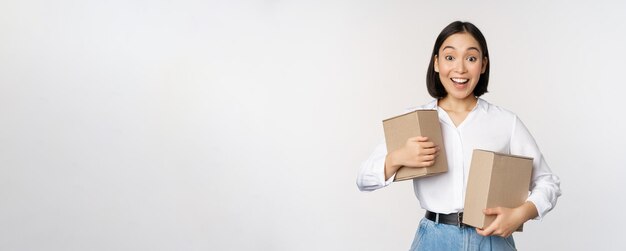 Retrato de uma garota coreana feliz segurando duas caixas e sorrindo olhando espantado com o conceito de câmera da loja