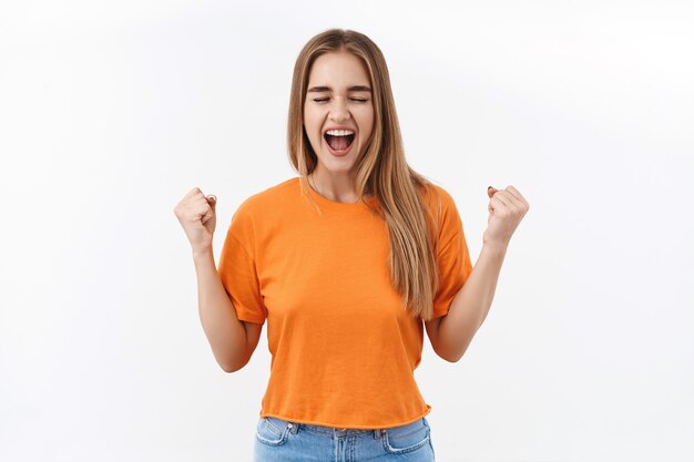 Retrato de uma garota feliz e sortuda, comemorando o sucesso, olhos fechados e sorrindo encantado