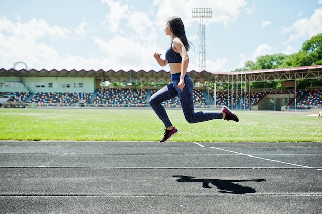 Retrato de uma garota forte em roupas esportivas correndo no estádio