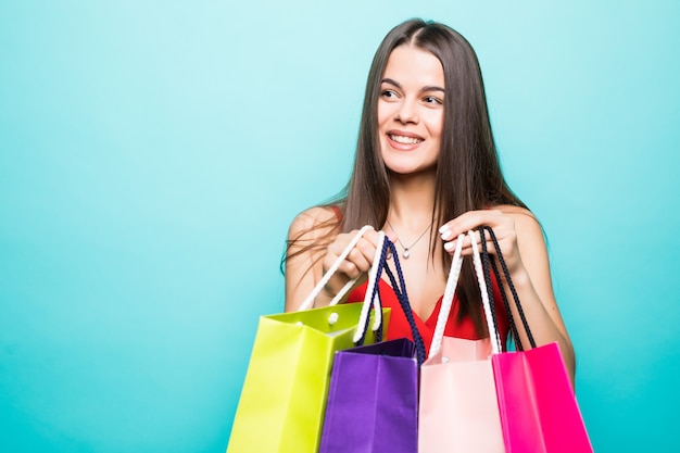 Retrato de uma garota linda e animada com vestido vermelho e óculos escuros segurando sacolas de compras isoladas sobre a parede azul