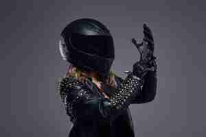 Foto grátis retrato de uma garota motociclista vestindo traje de piloto de couro e capacete protetor calçando luvas em um estúdio em um fundo cinza.
