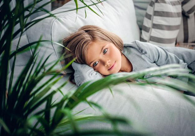 Retrato de uma garota posando em um sofá em uma sala de estar com plantas verdes.