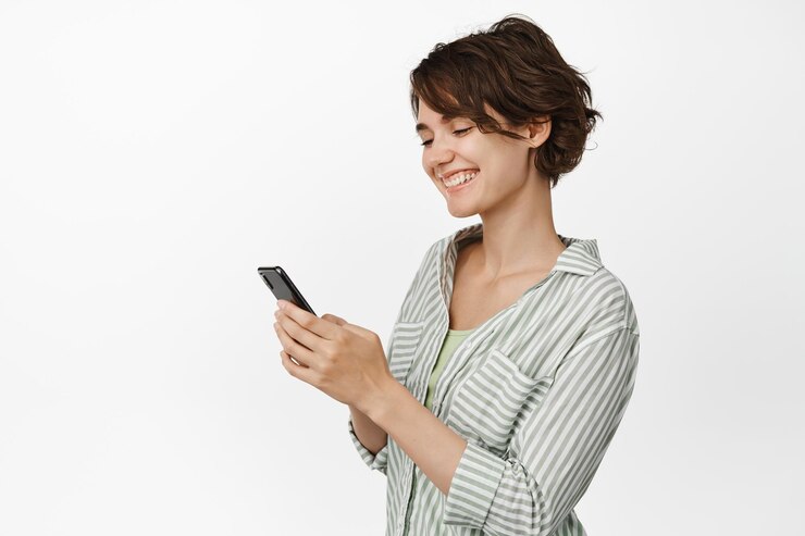 Foto grátis retrato de uma garota sorridente conversando no celular, usando celular smartphone, em traje casual contra fundo branco