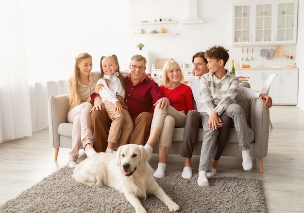 Retrato de uma grande família de várias gerações com seu cão de estimação sentado no sofá, sorrindo para a câmera, se divertindo em casa. lindos filhos com pais e avós passando tempo juntos dentro de casa