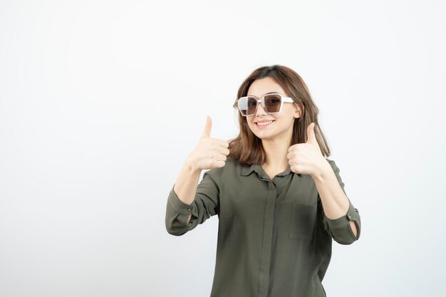 Retrato de uma jovem adorável em óculos dando polegares para cima. Foto de alta qualidade