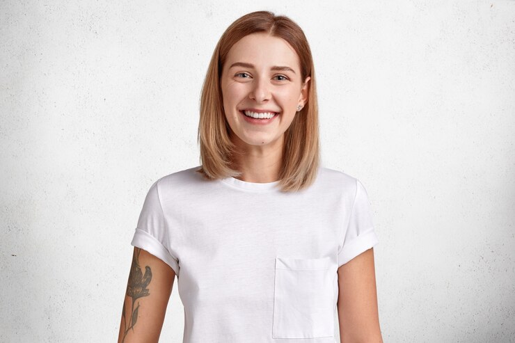Foto grátis retrato de uma jovem alegre, com cabelo curto, sorriso brilhante, tatuagem no braço, alegra-se com notícias positivas