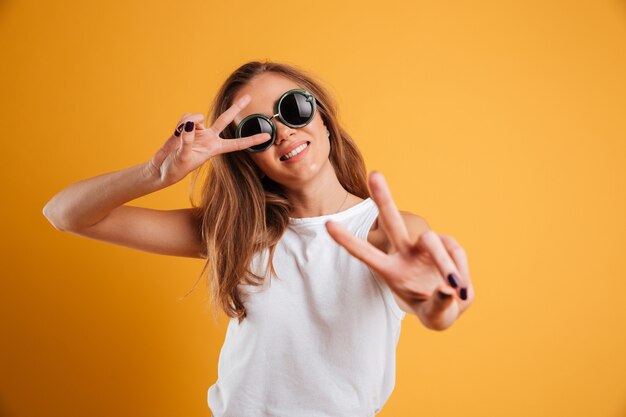 Retrato de uma jovem alegre em óculos de sol, mostrando a paz