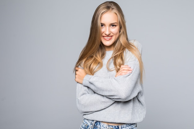 Retrato de uma jovem alegre em suéter sorrindo com os braços cruzados em um fundo cinza