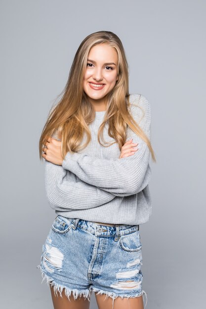 Retrato de uma jovem alegre em suéter sorrindo com os braços cruzados em um fundo cinza