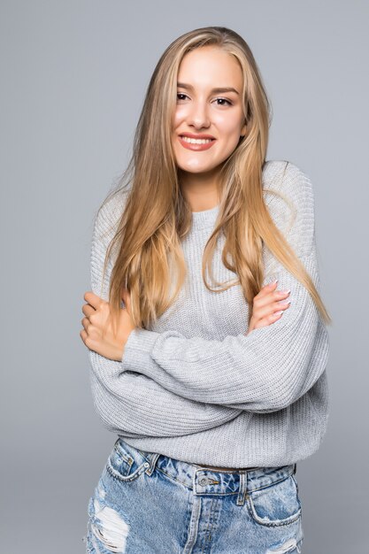 Retrato de uma jovem alegre em suéter sorrindo com os braços cruzados em um fundo cinza