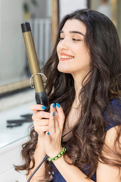 Retrato de uma jovem alegre segurando o secador de cabelo com as duas mãos e sorrindo