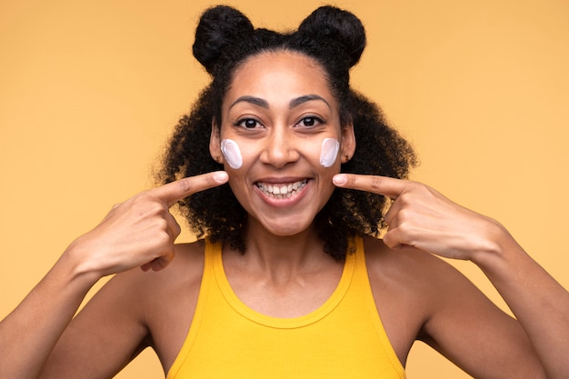 Foto grátis retrato de uma jovem apontando para as bochechas e tendo hidratante no rosto