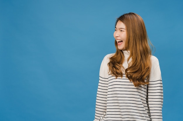 Retrato de uma jovem asiática com expressão positiva, sorriso amplo, vestida com roupas casuais sobre a parede azul