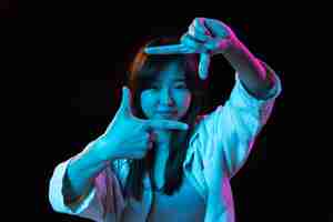 Foto grátis retrato de uma jovem asiática em fundo de estúdio escuro em neon conceito de emoções humanas expressão facial anúncio de vendas de jovens