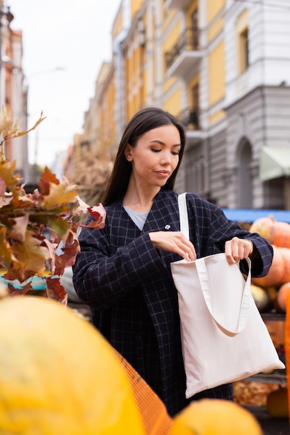 Foto grátis retrato de uma jovem atraente casual procurando bolsa na bolsa na loja de outono ao ar livre