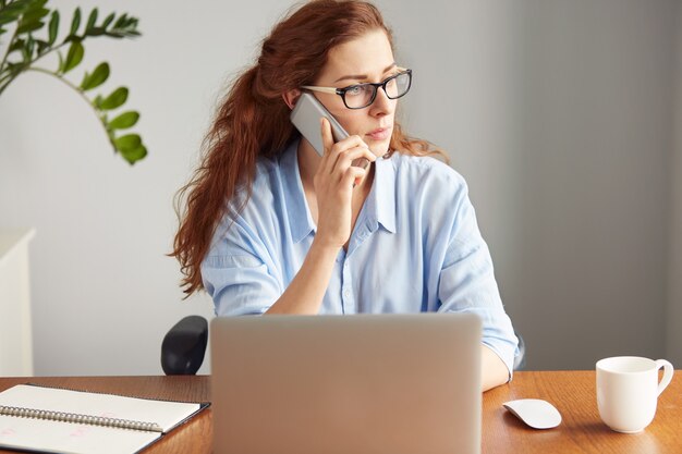 Retrato de uma jovem atraente falando ao celular e trabalhando no laptop