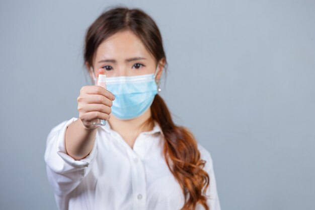 Retrato de uma jovem bela mulher de negócios usando máscara facial e aplicando álcool em spray na superfície cinza