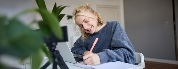 Foto grátis retrato de uma jovem blogueira de estilo de vida gravando um vídeo de si mesma fazendo anotações escrevendo em um diário