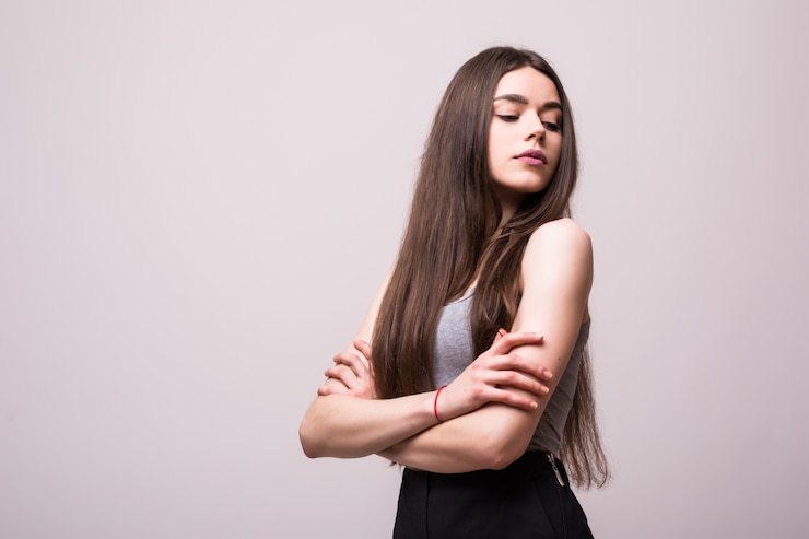 Foto grátis retrato de uma jovem bonita elegante sorrindo em uma camiseta cinza na parede branca, isolado, aparência natural, cabelos castanhos compridos, braços cruzados