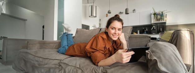 Retrato de uma jovem bonita relaxando em casa assistindo a um filme em um tablet digital ou lendo um ebook