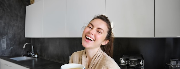 Foto grátis retrato de uma jovem bonita tomando café na cozinha aproveitando sua rotina matinal e