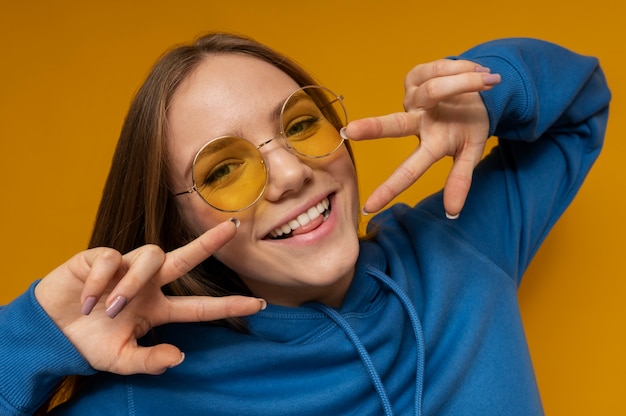 Retrato de uma jovem com óculos escuros e mostrando o símbolo da paz com as duas mãos