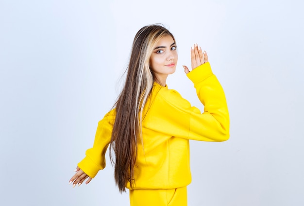 Retrato de uma jovem com roupa amarela em pé e posando sobre uma parede branca